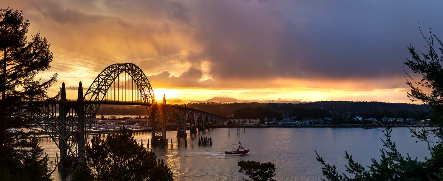 Yaquina bay bridge in newport, oregon at sunrise with a boat heading to sea