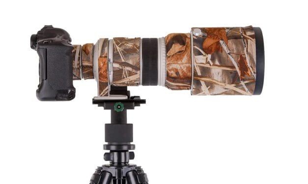 A Canon brand camera and lens with a LensCoat camouflage cover on a tripod