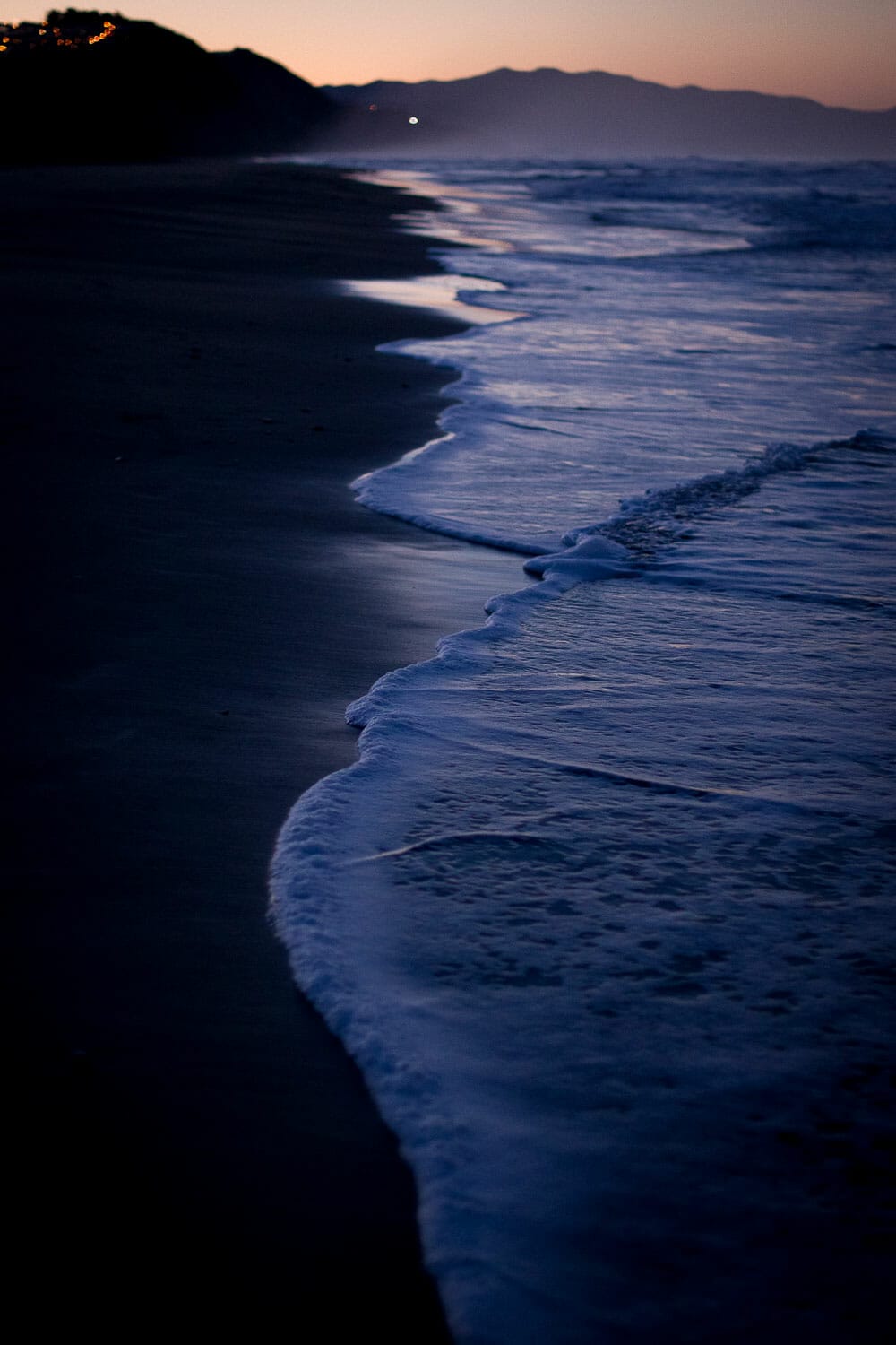 Twilight at the beach with gentle waves lapping the shore.
