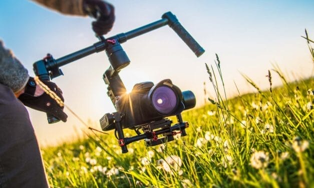 A filmmaker operating a camera on a stabilizing gimbal during a field shoot at sunset.